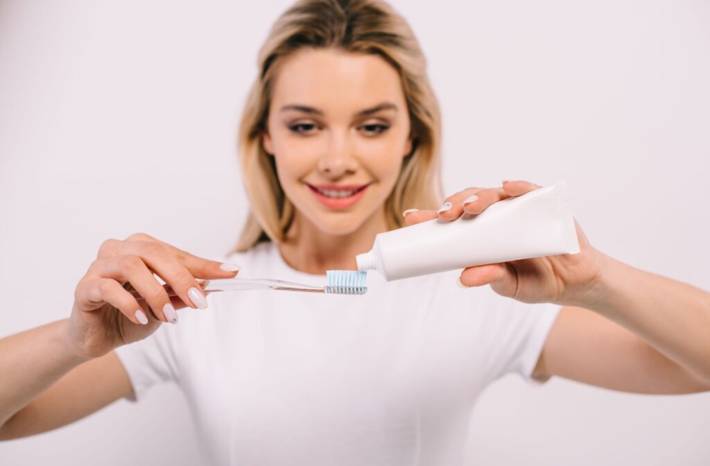 A woman smiling and applying toothpaste on a toothbrush.
