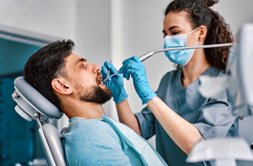 A dental hygienist cleans a man's teeth with professional dental equipment.
