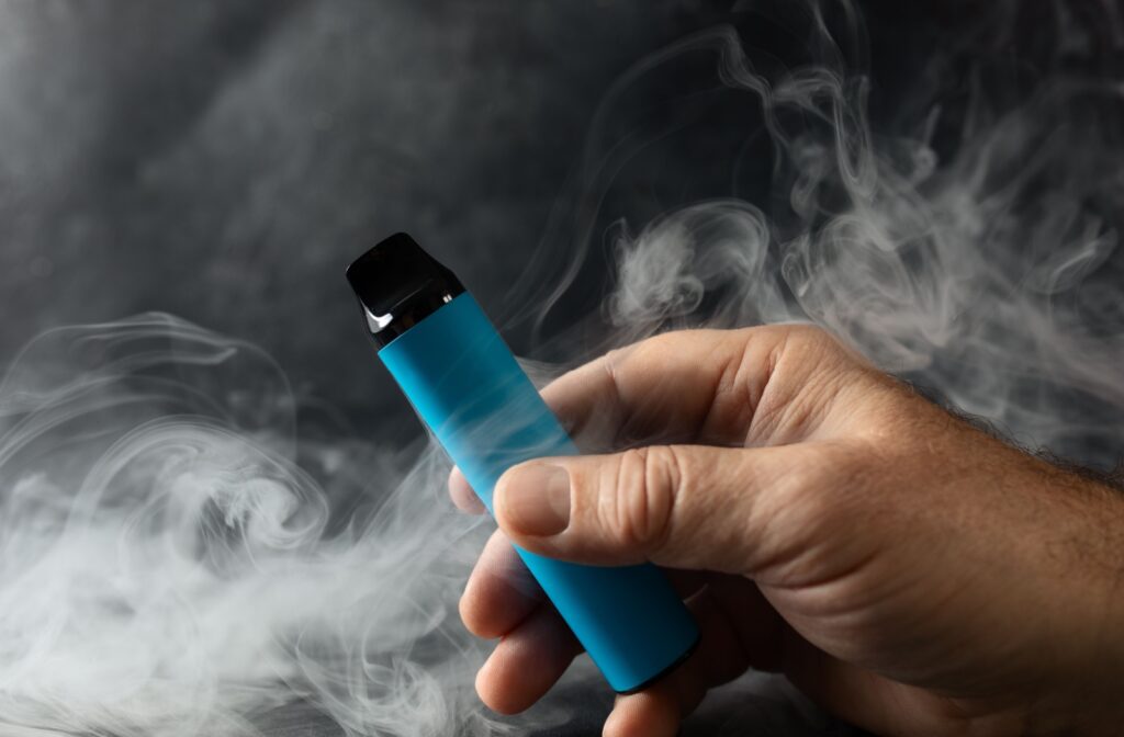 A hand holding a blue vape device with smoke wafting around