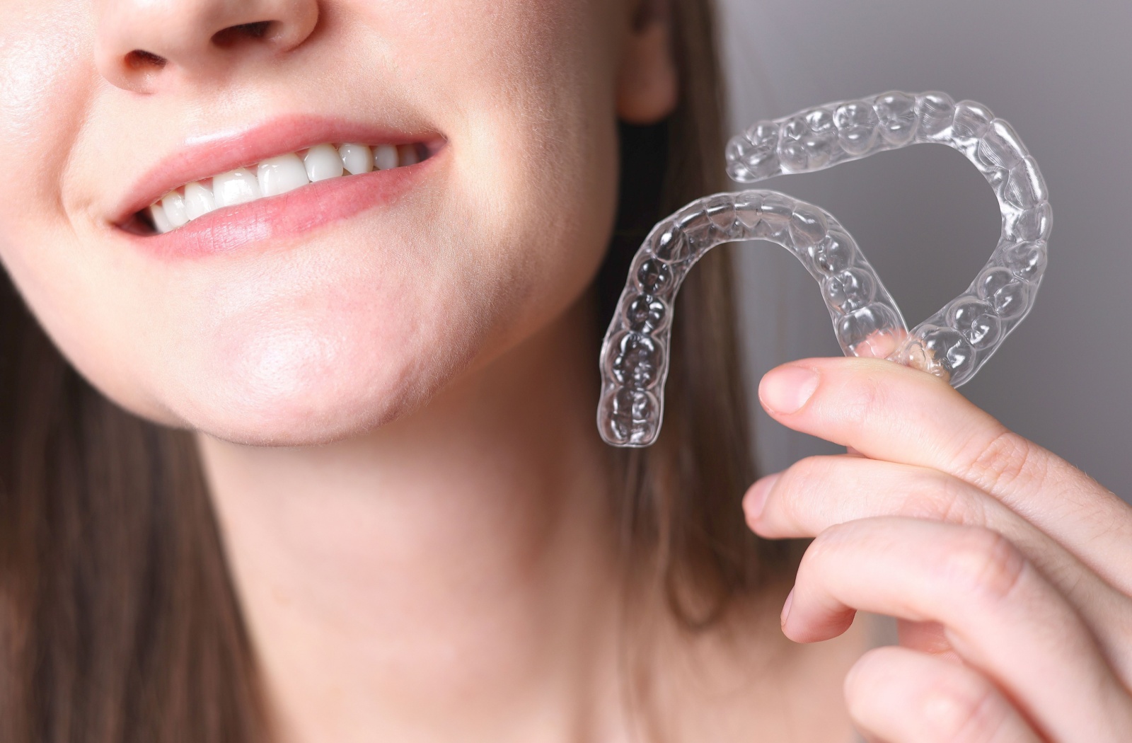 A smiling woman holding two clear aligners in her left hand.