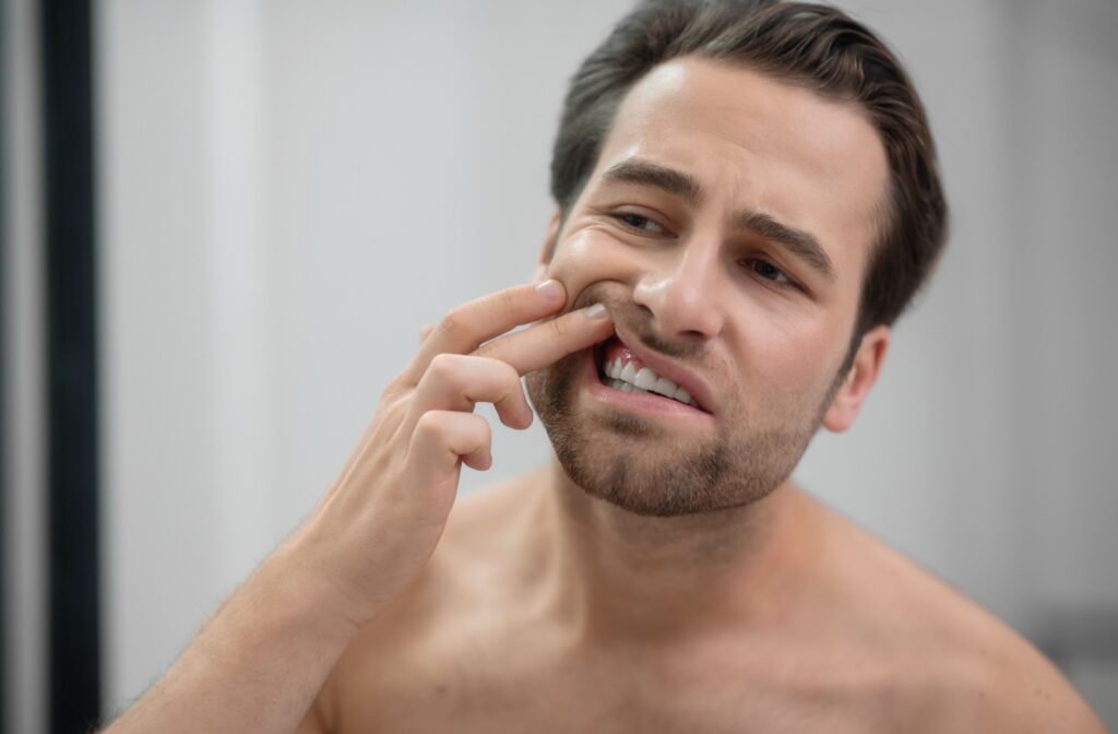 An adult lifting their lip with a finger to examine their gums in the mirror, looking for early signs of gum recession.