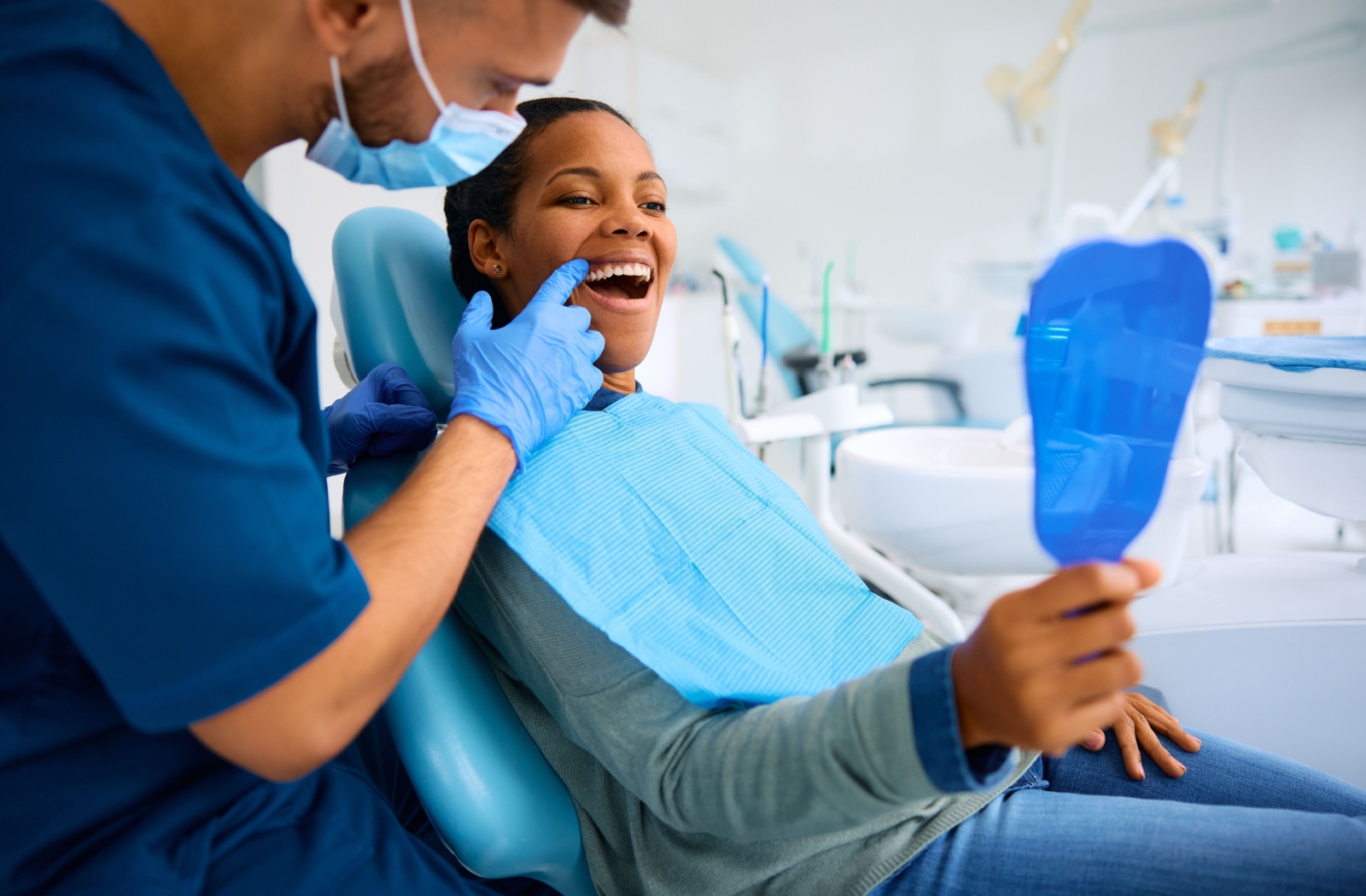 A patient smiling while their dentist gestures and shows the results of a dental exam and cleaning for gum recession.