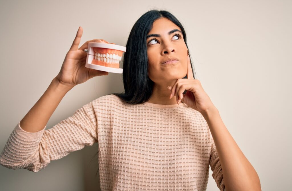 Woman holding a dental model looking thoughtful highlighting curiosity about dental health and oral care awareness