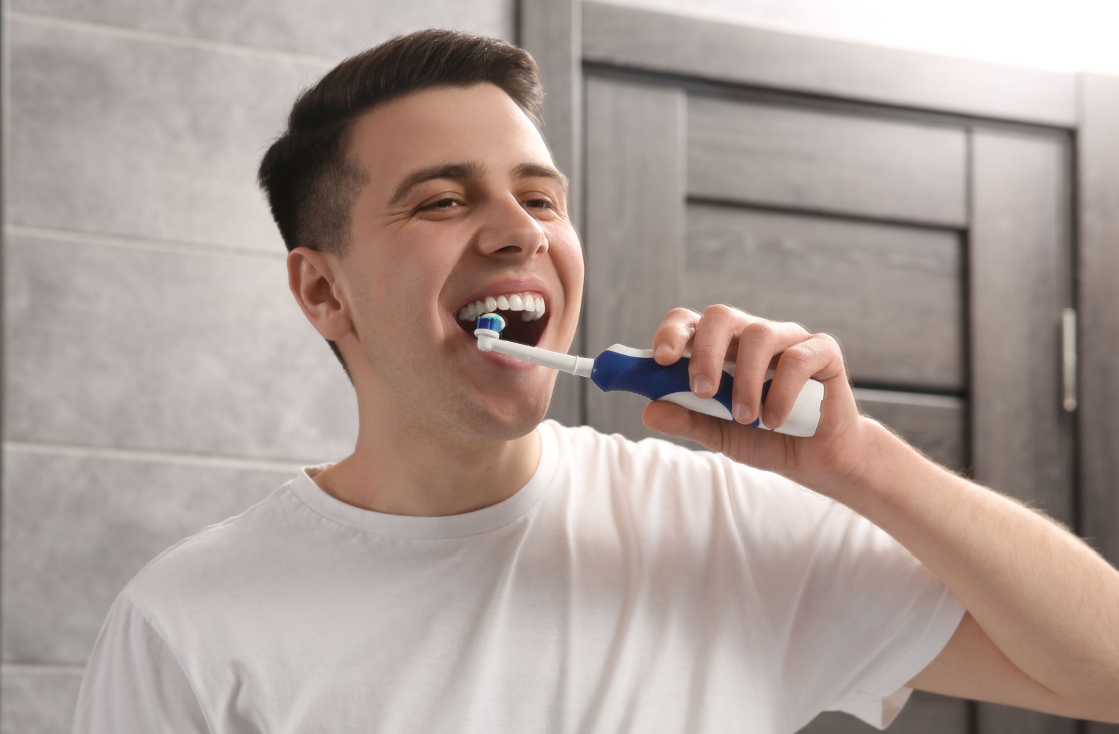 Young man using an electric toothbrush in a bathroom focusing on proper oral hygiene and healthy dental care habits