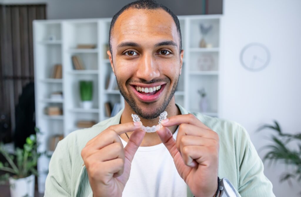 A smiling adult holds up their clear aligner before putting it in their mouth.