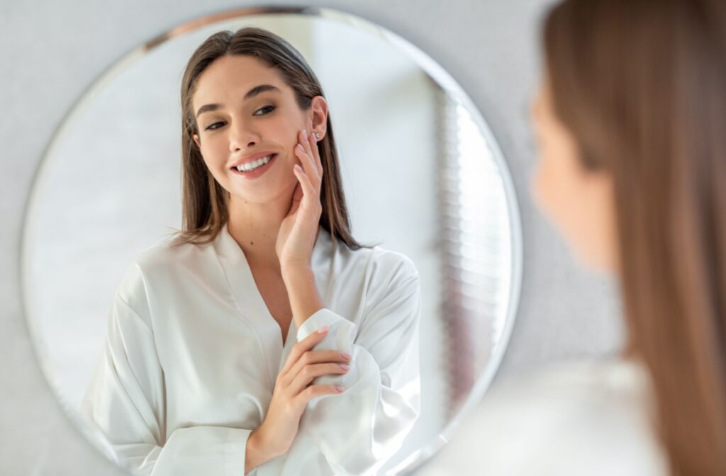 A woman in a white robe smiling at herself in the mirror.