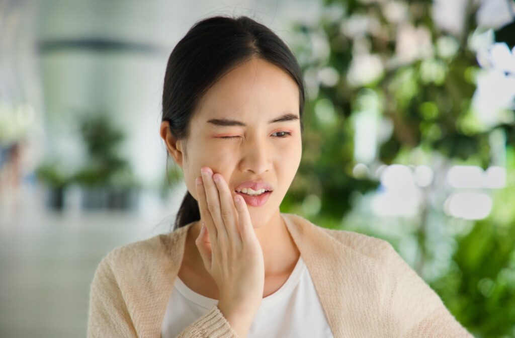 A person closes one eye and touches their cheek with a pained expression, showing discomfort possibly caused by a toothache.