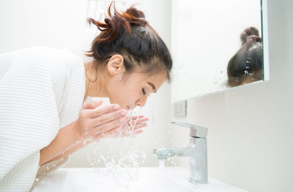 A person washing their face over the sink