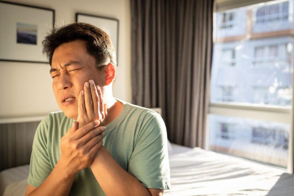 A man in his bedroom clutching his jaw in pain